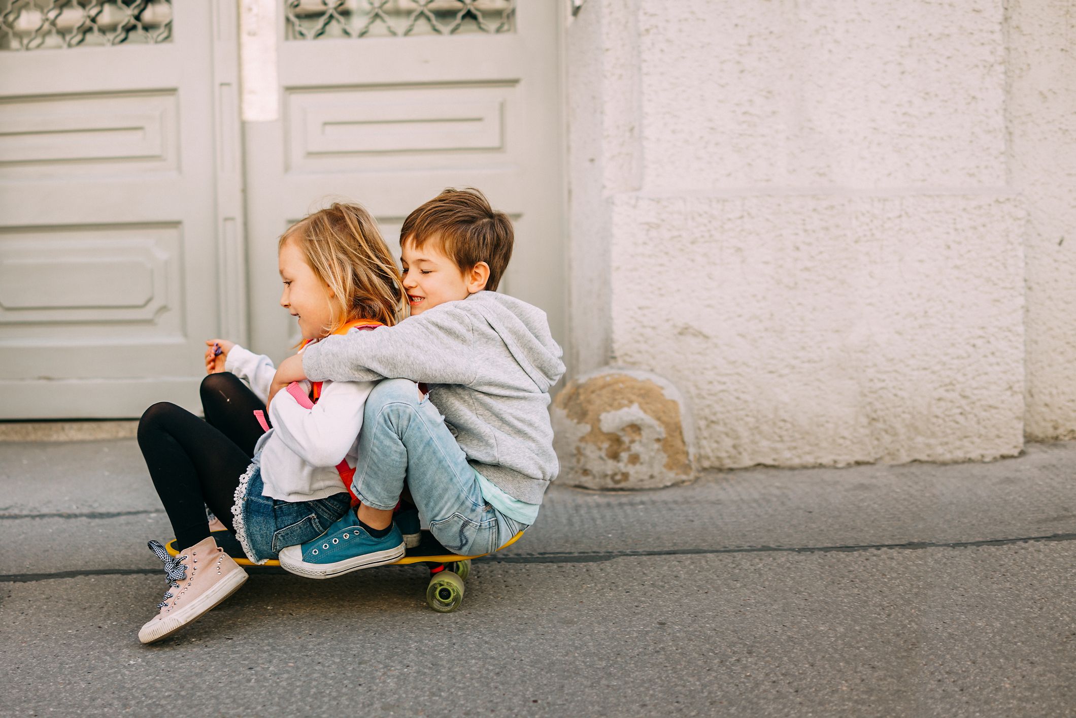 Zwei Kinder sitzen auf einem Skateboard auf der Straße