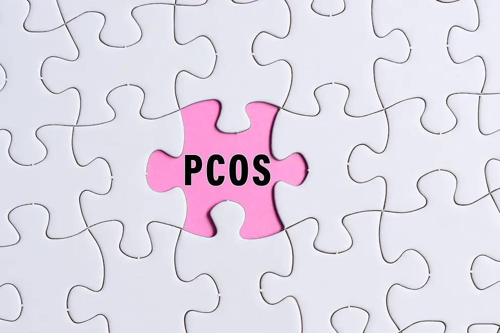 PCOS-Text auf weißem Puzzle über rosa Hintergrund.