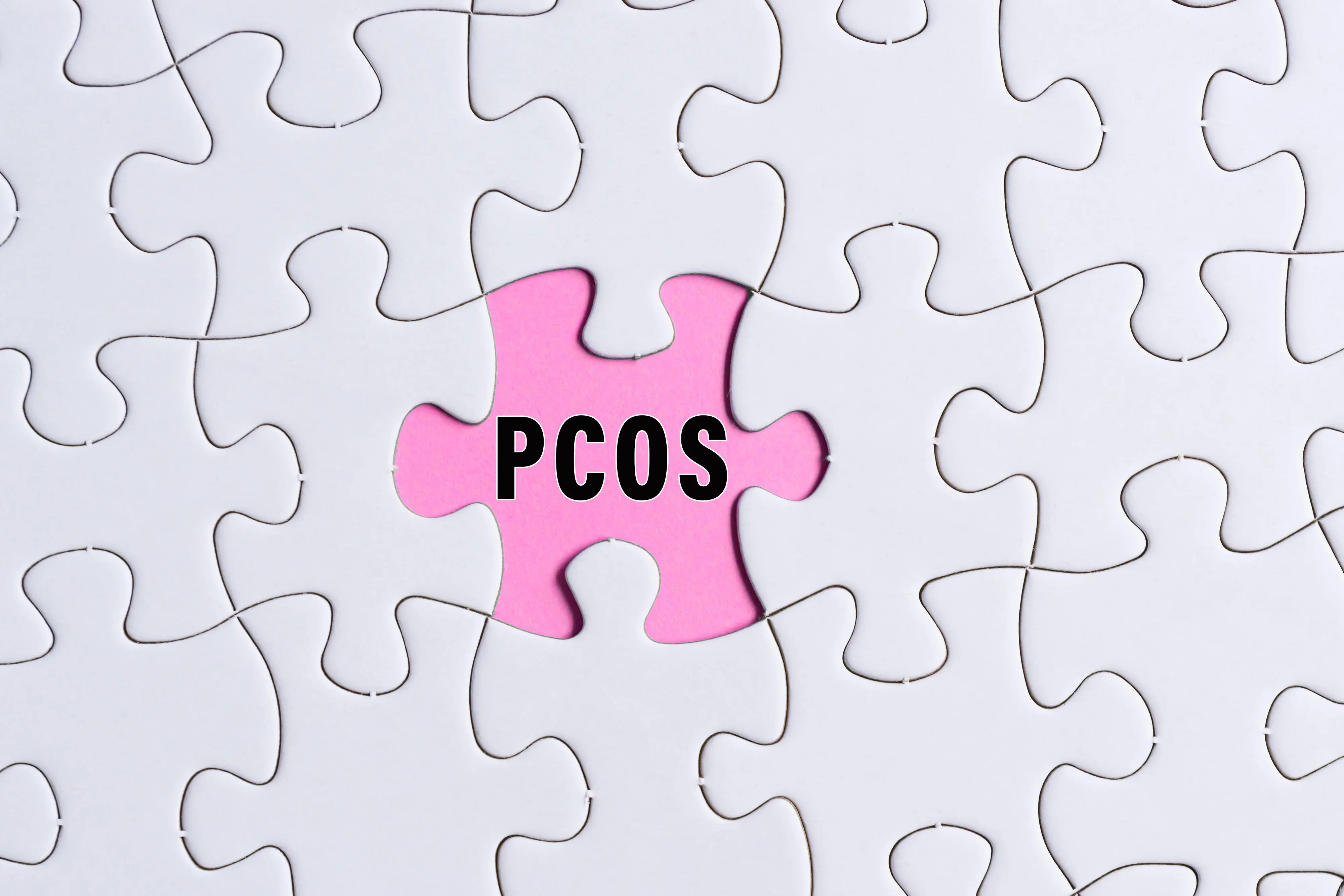 PCOS-Text auf weißem Puzzle über rosa Hintergrund.